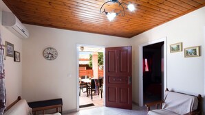 Una habitación con techo de madera, un reloj, un banco, una silla y una puerta que da a un comedor.