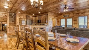 A wooden cabin interior with a dining area, kitchen, and a cozy seating area.