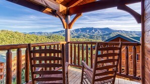A wooden balcony with a view of mountains and a building in the background.