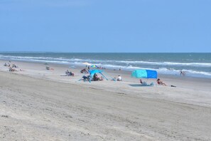 Uma praia com pessoas relaxando, guarda-sóis e uma tenda.
