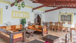 Ett mysigt rum med en soffa i trä, ett matbord och stolar. Det finns ett fönster med en dekorativ ram och en takfläkt.