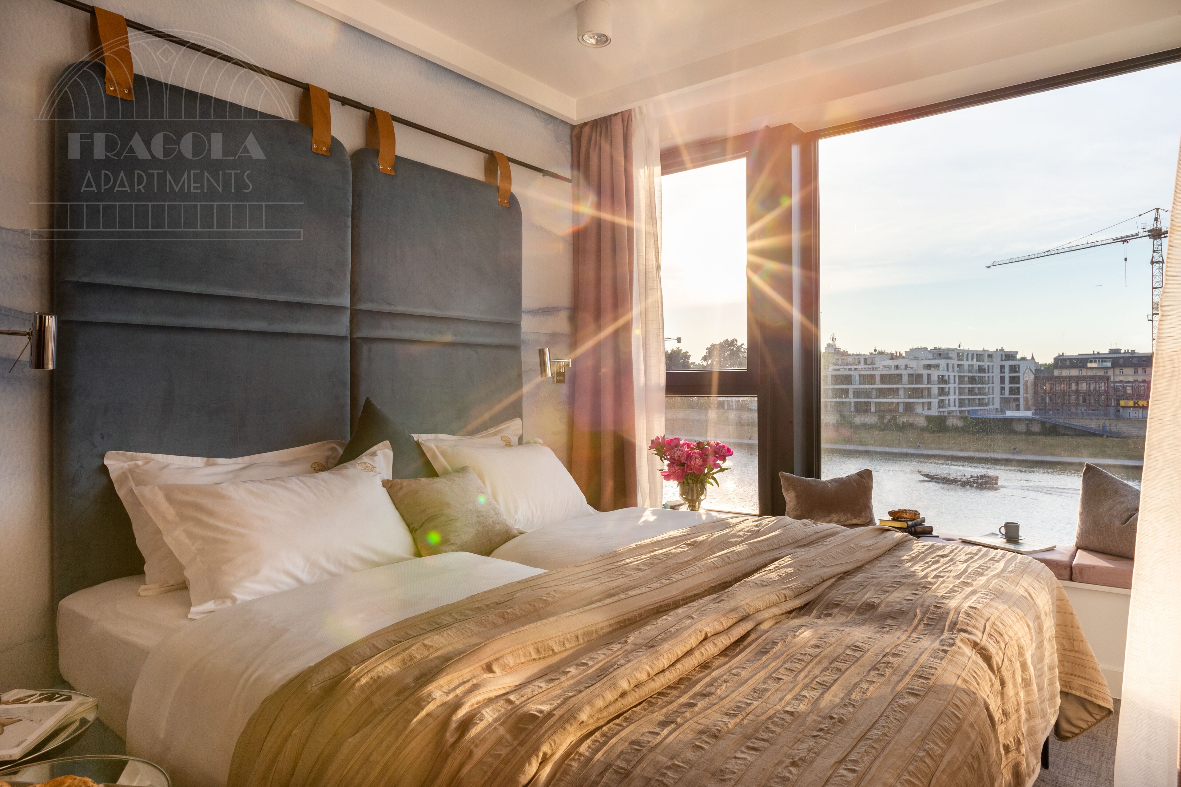 Un dormitorio moderno con una cama grande, vista a un río y un paisaje urbano al fondo.