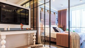A modern hotel room with a large TV, a glass coffee table with magazines, a bed with a view, and a large window. - Vistula View by Fragola Collection (Kraków)