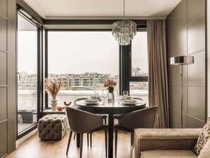 A dining area with a round table, chairs, a chandelier, and a view of buildings through large windows. - Vistula View by Fragola Collection (Kraków)