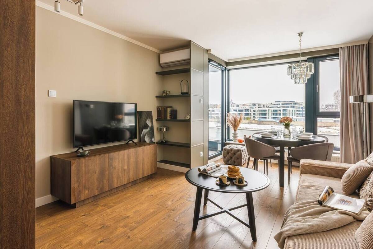 Una sala de estar moderna con una televisión de pantalla plana, piso de madera, un comedor con una mesa redonda y un sofá.