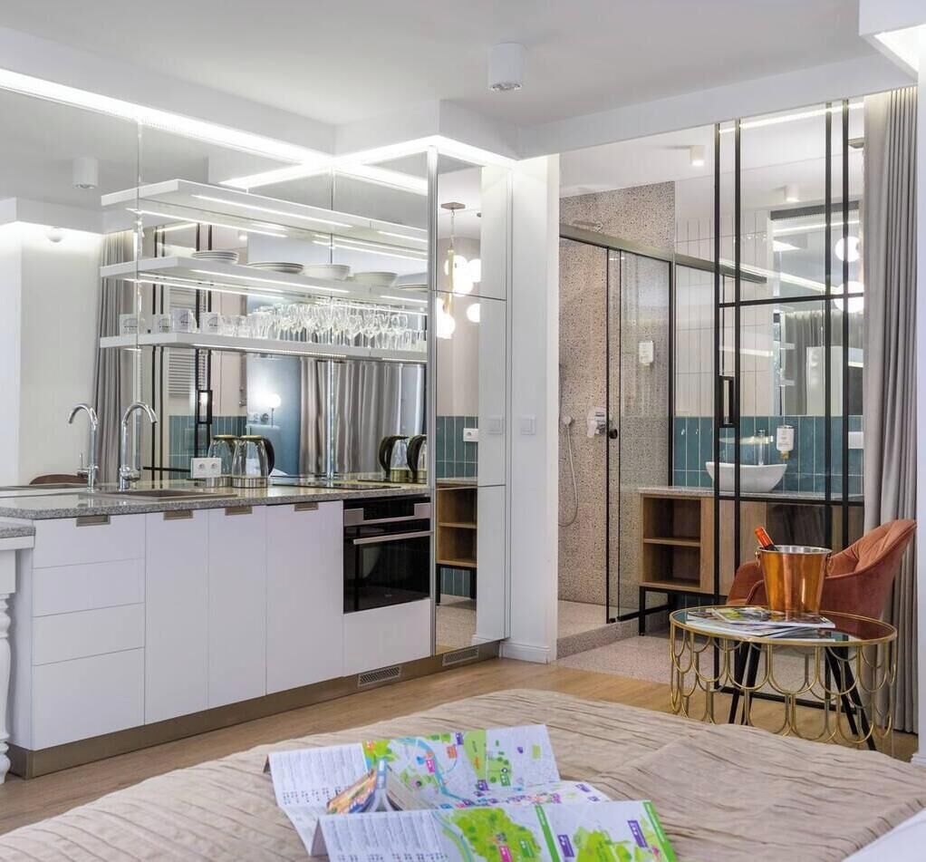 A modern kitchen with a central island, a dining area with a table and chairs, and a view of the bathroom through a glass partition.