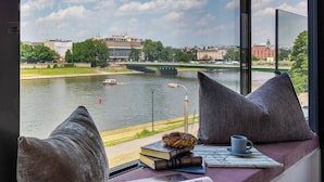 A view from a window with a river, a bridge, and buildings in the background. - Vistula View by Fragola Collection (Kraków)