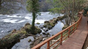 A wooden boardwalk beside a river with rocky banks and trees. - Amazing paradise Una (Donji Lapac)