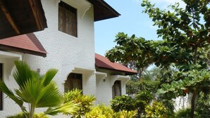 A white building with a red roof, surrounded by various potted plants and trees. - Malaika House (Malindi)