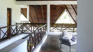 A covered outdoor area with a wooden railing, a seating area with a patterned cushion, and a view of greenery outside. - Malaika House (Malindi)