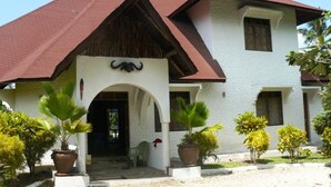 A two-story building with a red roof, a central entrance with an archway, and potted plants in front. - Malaika House (Malindi)