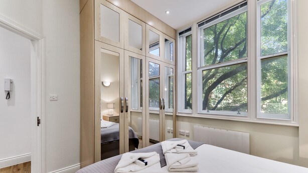 Moderni hotellihuone, jossa on suuri sänky, erillinen vaatehuone ja ikkunasta avautuva näkymä puistoon.