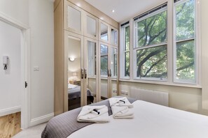 A modern hotel room with a large bed, a walk-in closet, and a view of trees through the window. - Cosy 1 Bed Apartment next to Liverpool Street Station FREE WIFI By City Stay Aparts London (London)