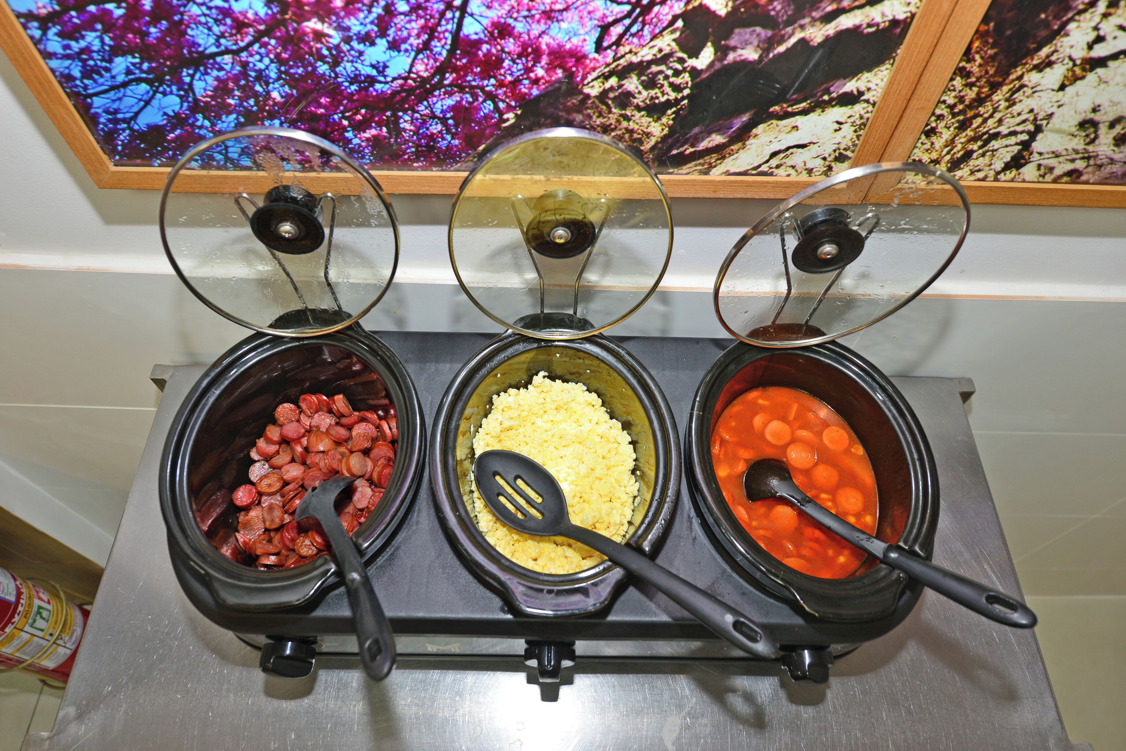 Three slow cooker dishes with lids, a spoon in each, and a wooden-framed picture above.