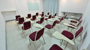 Une salle de conférence avec des rangées de chaises et de tables, un tableau blanc et une fenêtre avec des rideaux.
