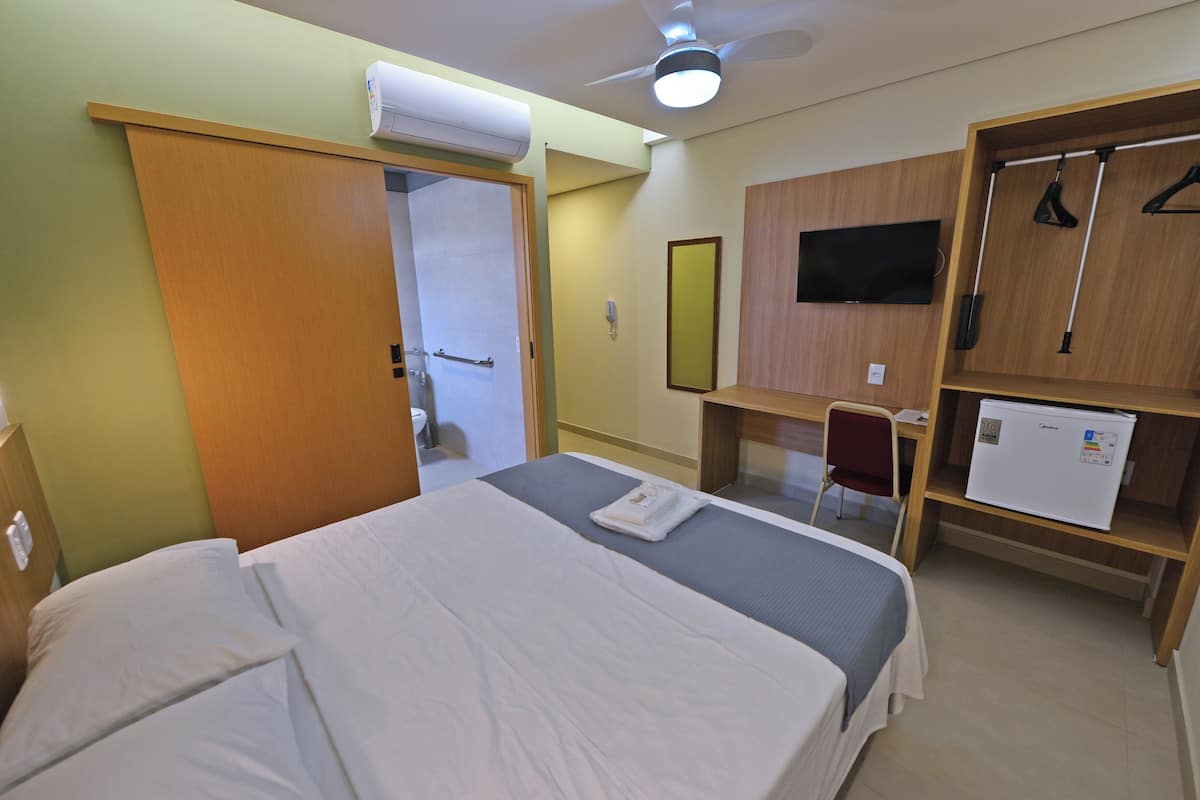 Ein Hotelzimmer mit einem Bett, einem Schreibtisch, einem Stuhl, einem Kleiderschrank, einem Fernseher und einem Kühlschrank.