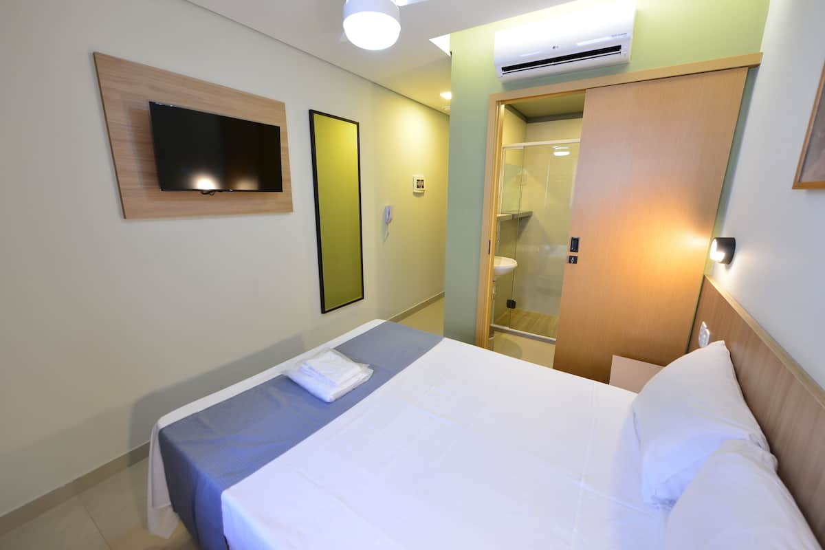 Ein Hotelzimmer mit Bett, Wandfernseher, Spiegel und einer Tür zu einem Badezimmer.