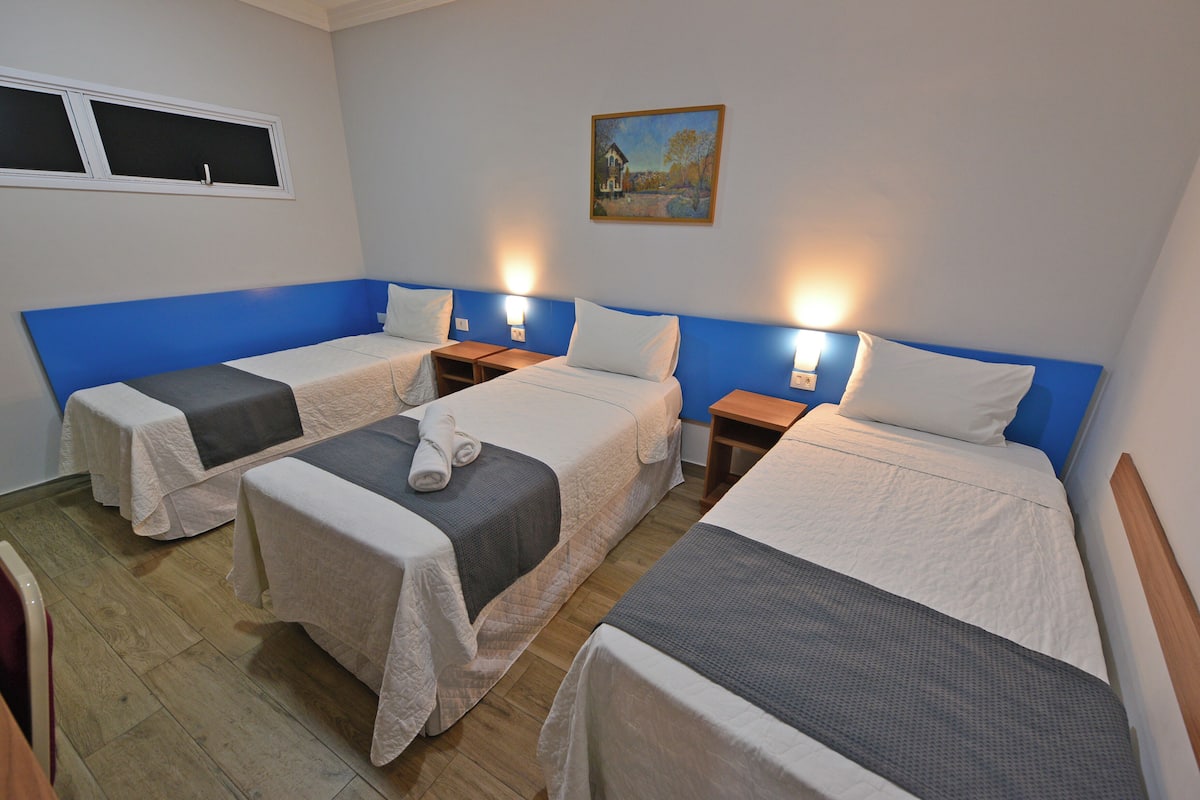Ein Hotelzimmer mit drei Betten, einem Bild an der Wand und einem Fenster.