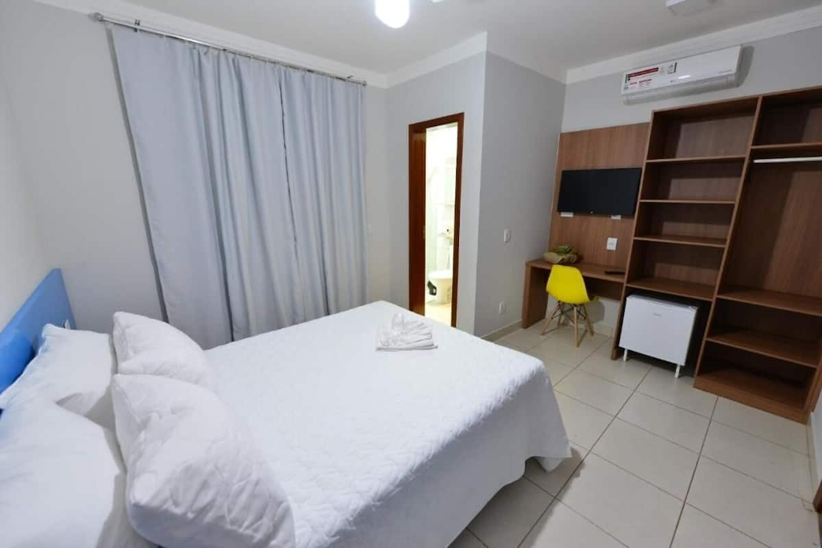 Ein Hotelzimmer mit Bett, Schreibtisch, Stuhl, Kleiderschrank und Klimaanlage.
