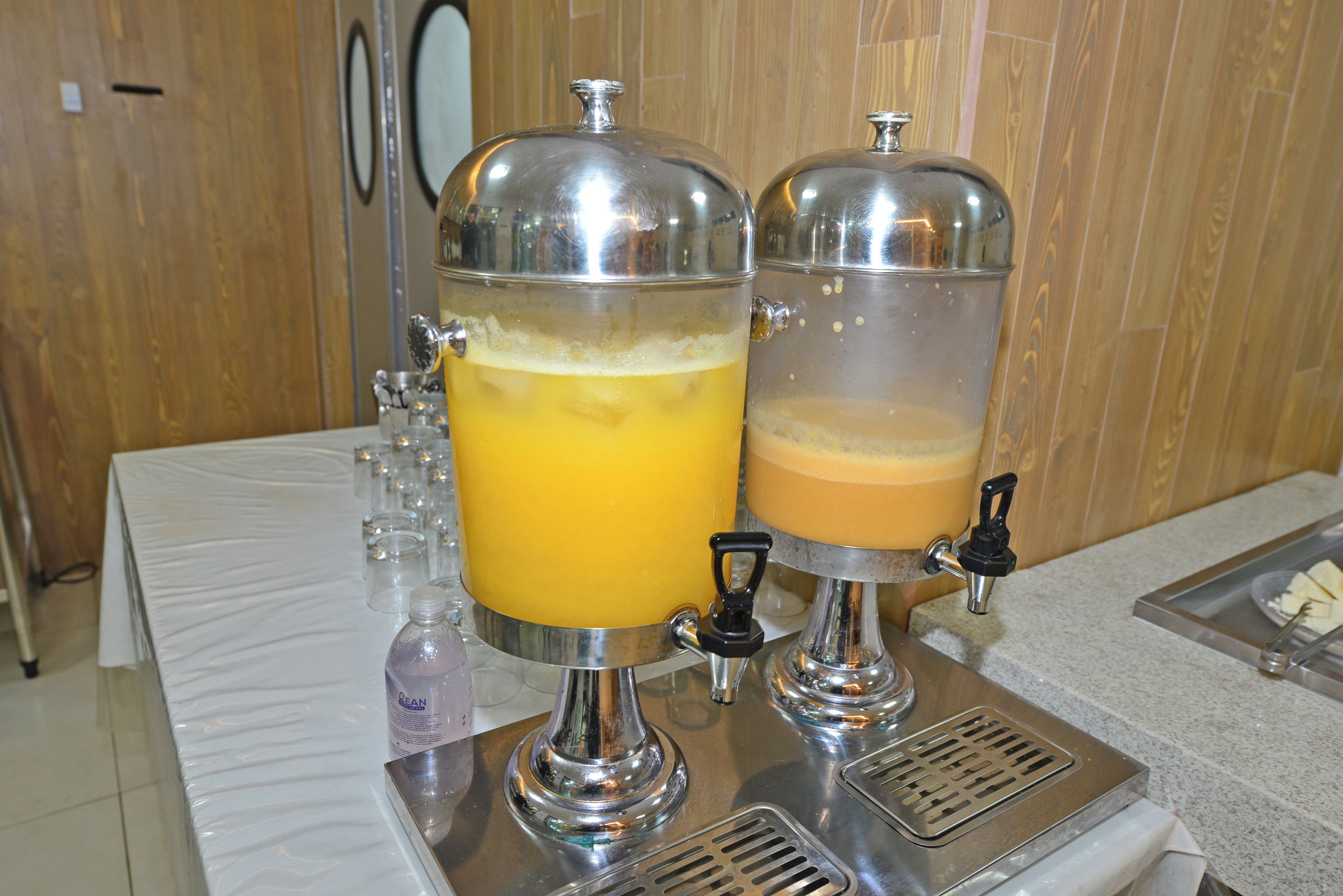 Un dispensador de bebidas con dos contenedores transparentes, uno con líquido amarillo y otro con líquido marrón, ambos con grifos para servir.