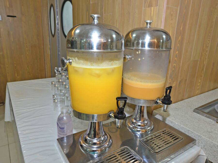 Un dispensador de bebidas con dos contenedores transparentes, uno con líquido amarillo y otro con líquido marrón, ambos con grifos para servir.