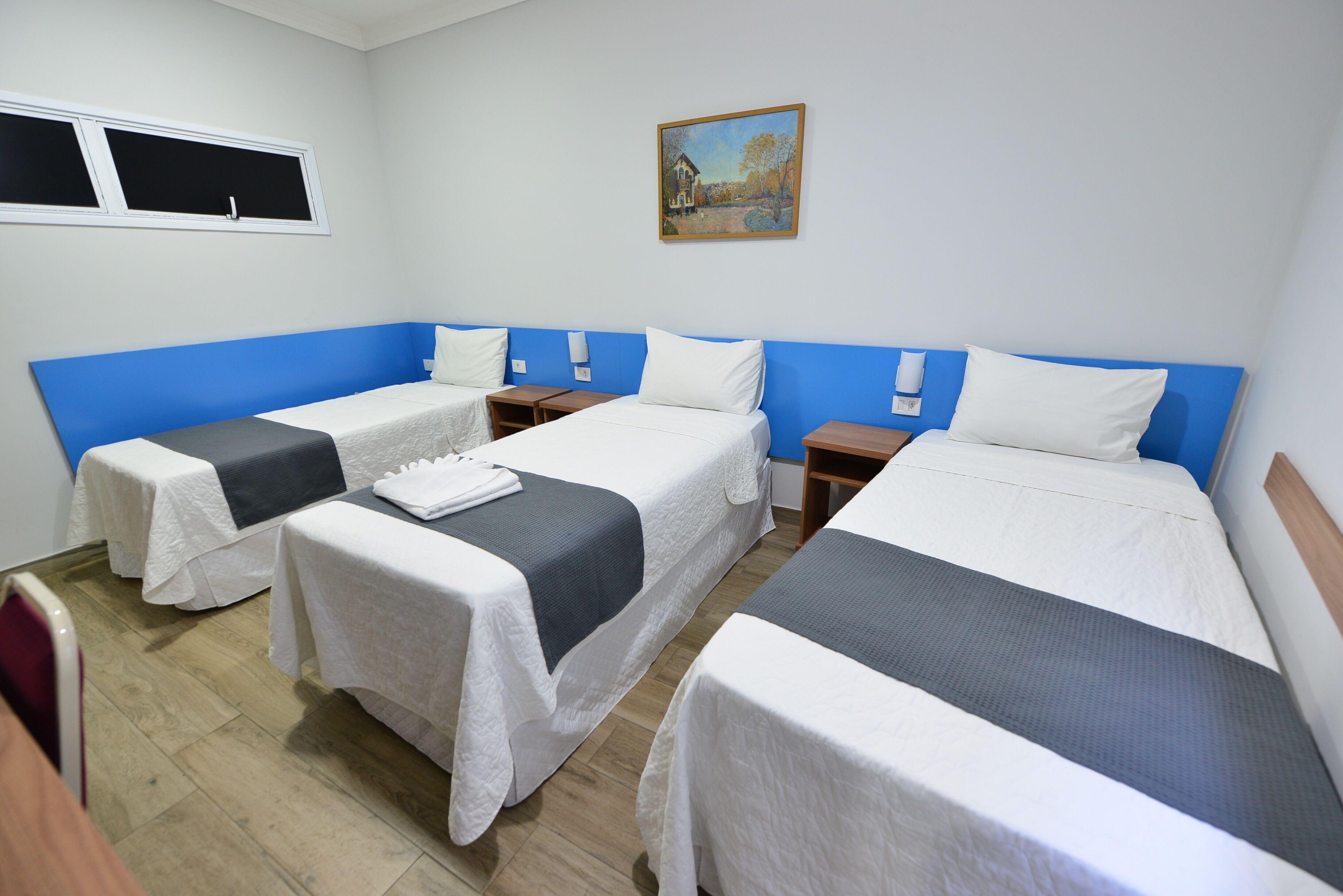 Quarto de hotel com quatro camas de solteiro, um quadro na parede e uma janela.