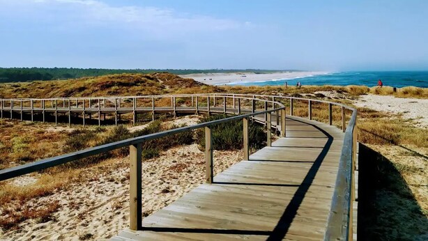 A wooden boardwalk leading to a beach with a clear view of the ocean and dunes in the background. - Home Sweet Home - Entire Apartament (Ovar)