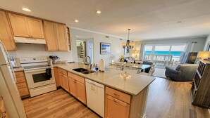 A spacious kitchen with wooden cabinets, a central island, and a view of the ocean. - Queen's Grant E-117 – Perfect Beach Getaway (Topsail Beach)