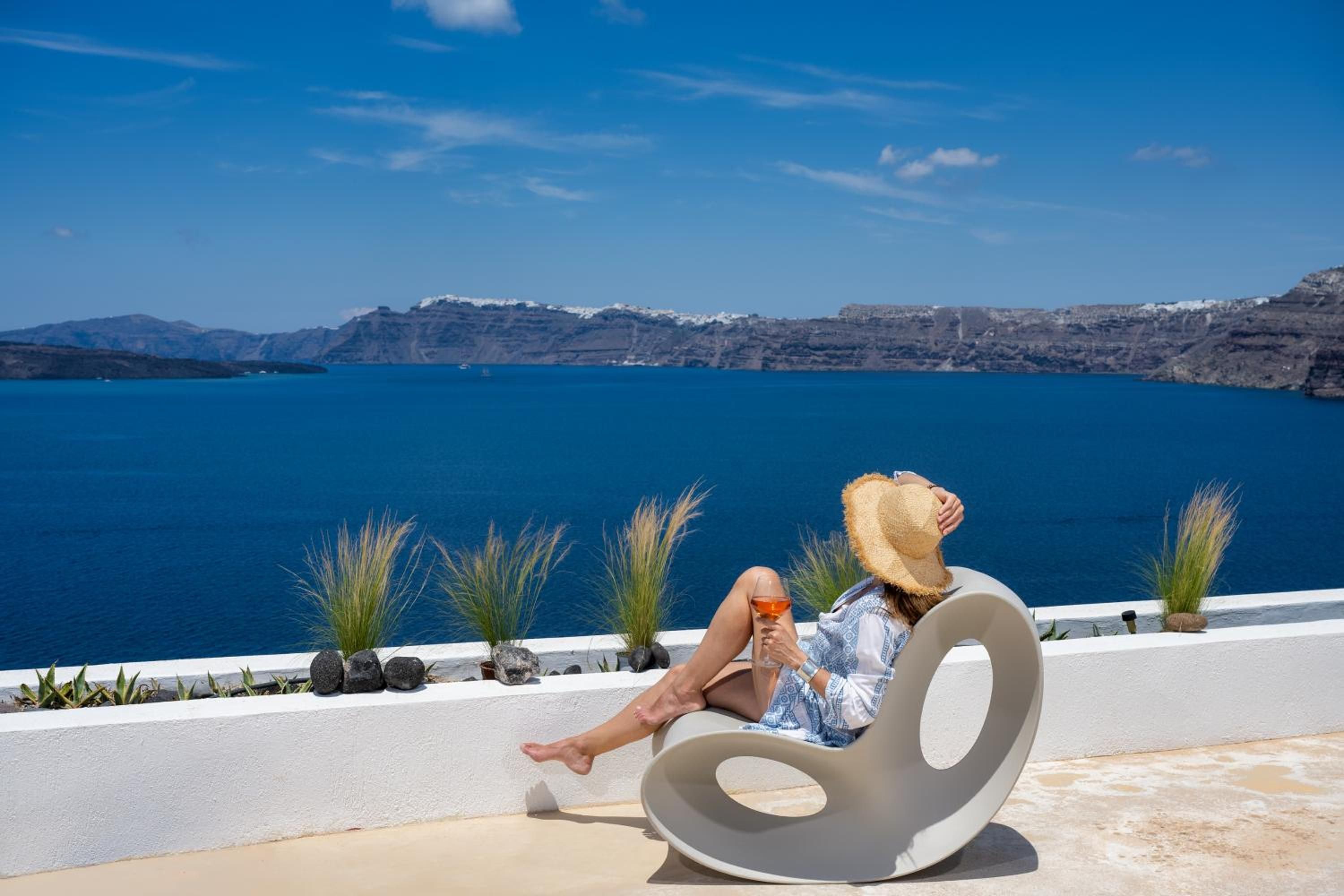 A person relaxing on a curved white chair with a view of a large body of water and distant mountains.