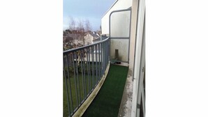 A balcony with a metal railing, a small patch of artificial grass, and a white wall in the background. - Appartement Le Conquérant - Caen (Caen)