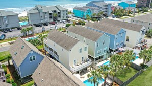 Un quartier résidentiel situé sur la côte, composé de plusieurs immeubles à deux étages, d’une piscine et d’une plage en arrière-plan.