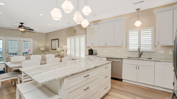 Une cuisine moderne avec des meubles blancs, un îlot en marbre et des luminaires suspendus.