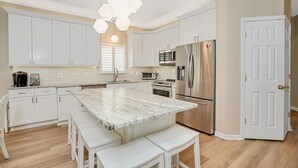 Une cuisine moderne avec des meubles blancs, un îlot en marbre, des appareils électroménagers en acier inoxydable et un luminaire suspendu.