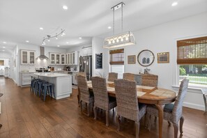 A modern kitchen with white cabinets, a central island, and a dining area with wicker chairs and a wooden table.