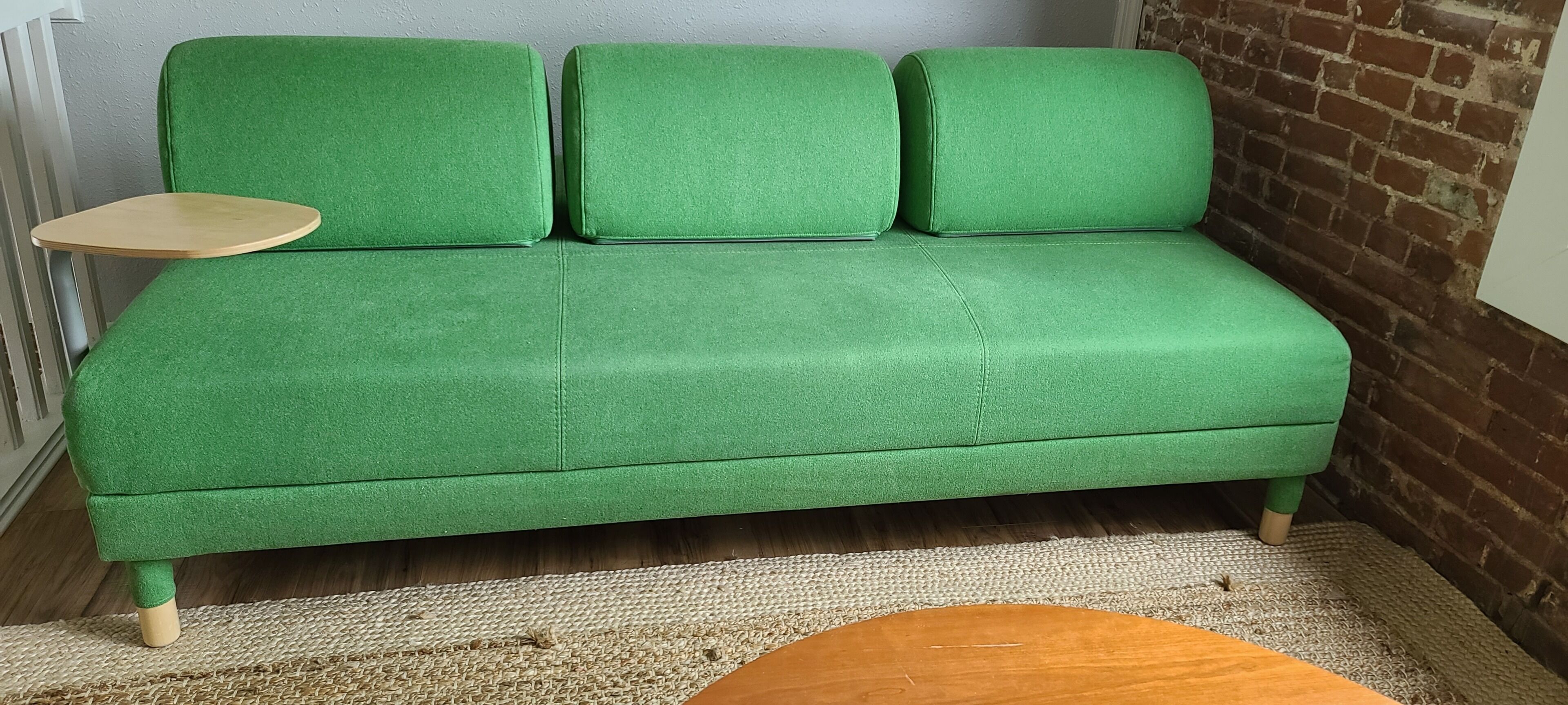 Um sofá verde com uma mesinha de madeira num canto de um quarto com parede de tijolos e soalho de madeira.