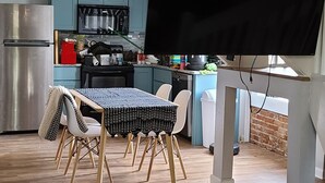 Un'ampia zona giorno con pavimento in legno, un tavolo da pranzo con sedie, una cucina sullo sfondo e una scala con ringhiere bianche.