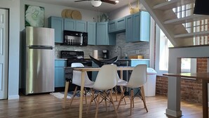 Una cucina moderna con mobili color petrolio, elettrodomestici in acciaio inossidabile e un'area pranzo con sedie bianche.