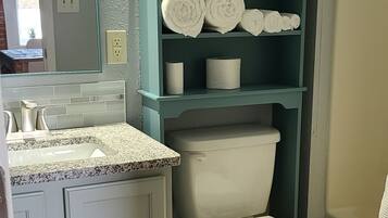 A bathroom with a toilet, sink, and shelves with towels.