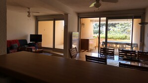 Amplia sala de estar con un gran ventanal corredero que da a un balcón, una mesa de comedor con sillas y un ventilador de techo.