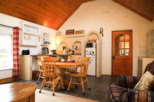 A cozy kitchen with wooden cabinets, a dining table with chairs, a refrigerator, and a wooden ceiling.