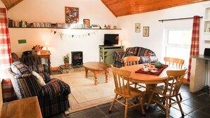 Ein gemütliches Wohnzimmer mit Kamin, Fernseher, Essbereich mit Holzkohle und Bücherregal mit Büchern und Dekorationen.