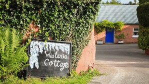 Ein Schild mit der Aufschrift 'Wisteria Cottage', im Hintergrund ein Backsteinhaus und eine blaue Tür.