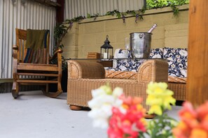 A wicker sofa with a floral cushion, a wooden rocking chair, and a metal bucket on a table.