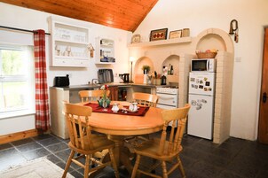 A kitchen with a round wooden table, four wooden chairs, a white refrigerator, and a microwave.
