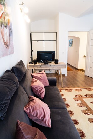 A modern living room with a dark grey sofa, pink cushions, a wooden coffee table, a black monitor, and a patterned rug.