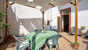 Une terrasse avec une table et des chaises, protégée par un auvent et entourée de plantes en pot.