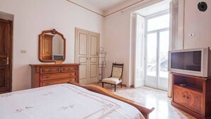 Une chambre à coucher comprenant un lit, une commode, un miroir, une chaise et un téléviseur.