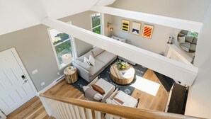 Un loft spacieux avec un plafond haut, un escalier, un espace de vie comprenant un canapé, une table basse et des œuvres d’art.