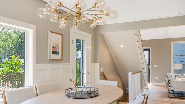 Un espace repas avec une table ronde, des chaises et un lustre. Un escalier mène à un niveau supérieur.