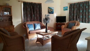 A living room with wicker furniture, a flat-screen TV, and artwork on the walls. - Villa The Golden Dream  (Flic en Flac)